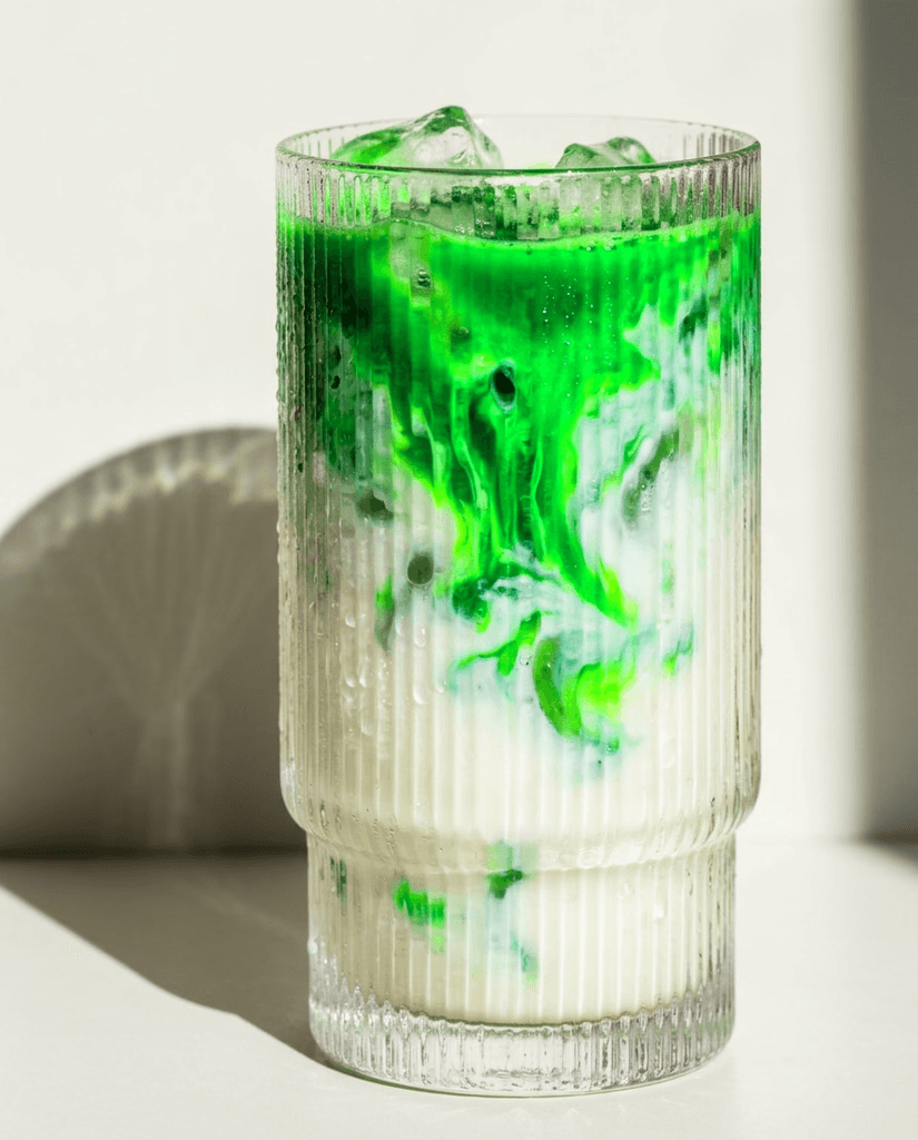 Iced matcha swirling into milk in a ribbed glass